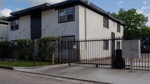 Een gebouw met twee verdiepingen, een zwart metalen hek, een brievenbus en een kleine tuin.