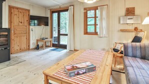 Une pièce chaleureuse avec un plancher en bois, un canapé, une table sur laquelle se trouve une boîte de jeux de puzzle, un téléviseur et une fenêtre avec des rideaux.