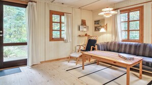Une pièce chaleureuse avec un plancher en bois, un canapé, un fauteuil, une table et de grandes fenêtres avec des rideaux.