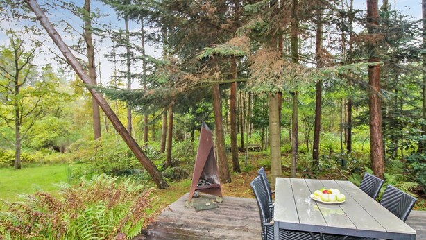 Une terrasse extérieure en bois, avec une table et des chaises, entourée d’une zone boisée.