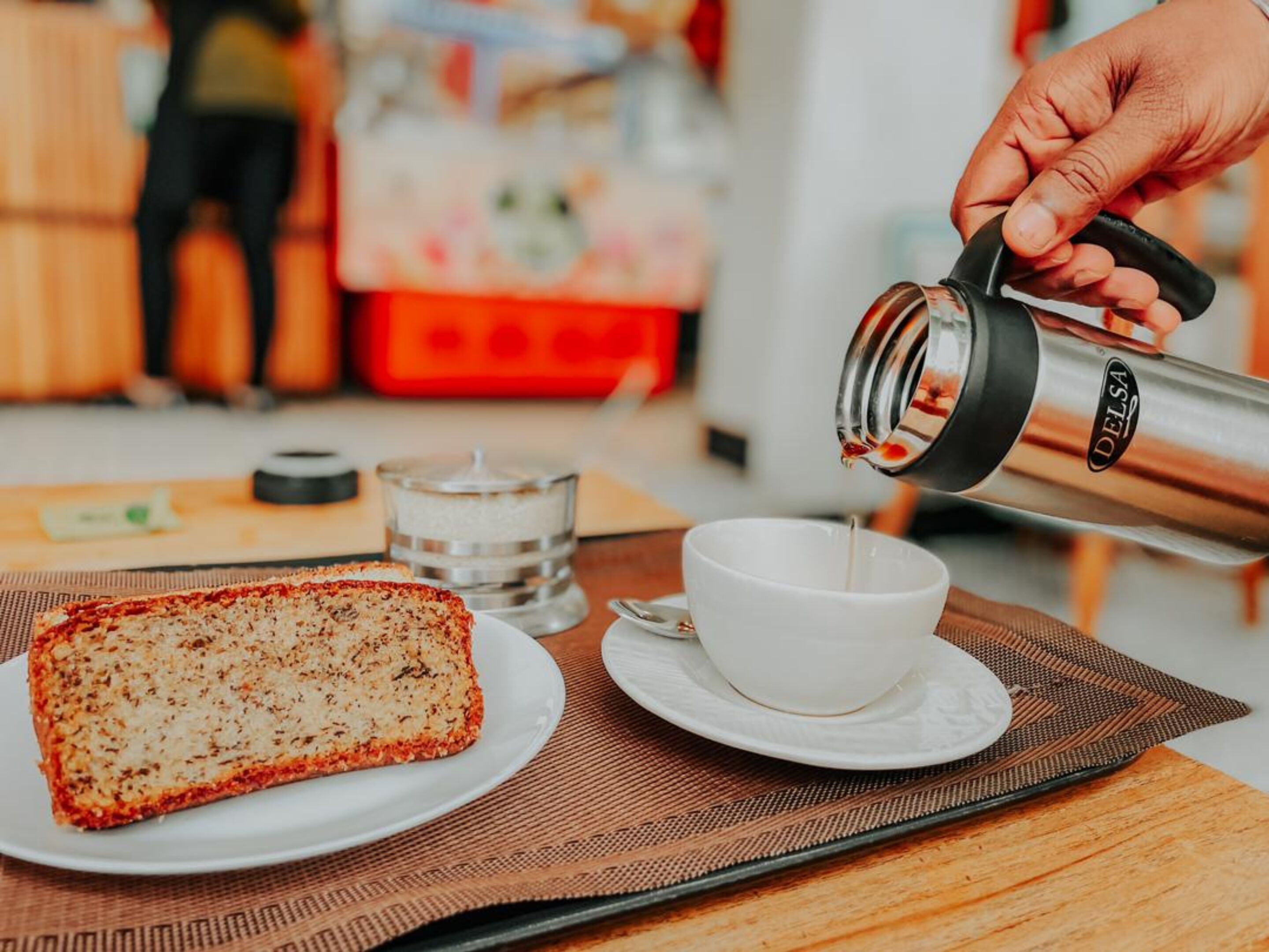 Uma pessoa servindo café em uma xícara sobre uma mesa com um pão e uma vela.