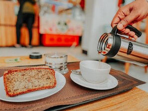 A person pouring coffee into a cup on a table with a loaf of bread and a candle. - The Baobab Home stay (Dodoma)