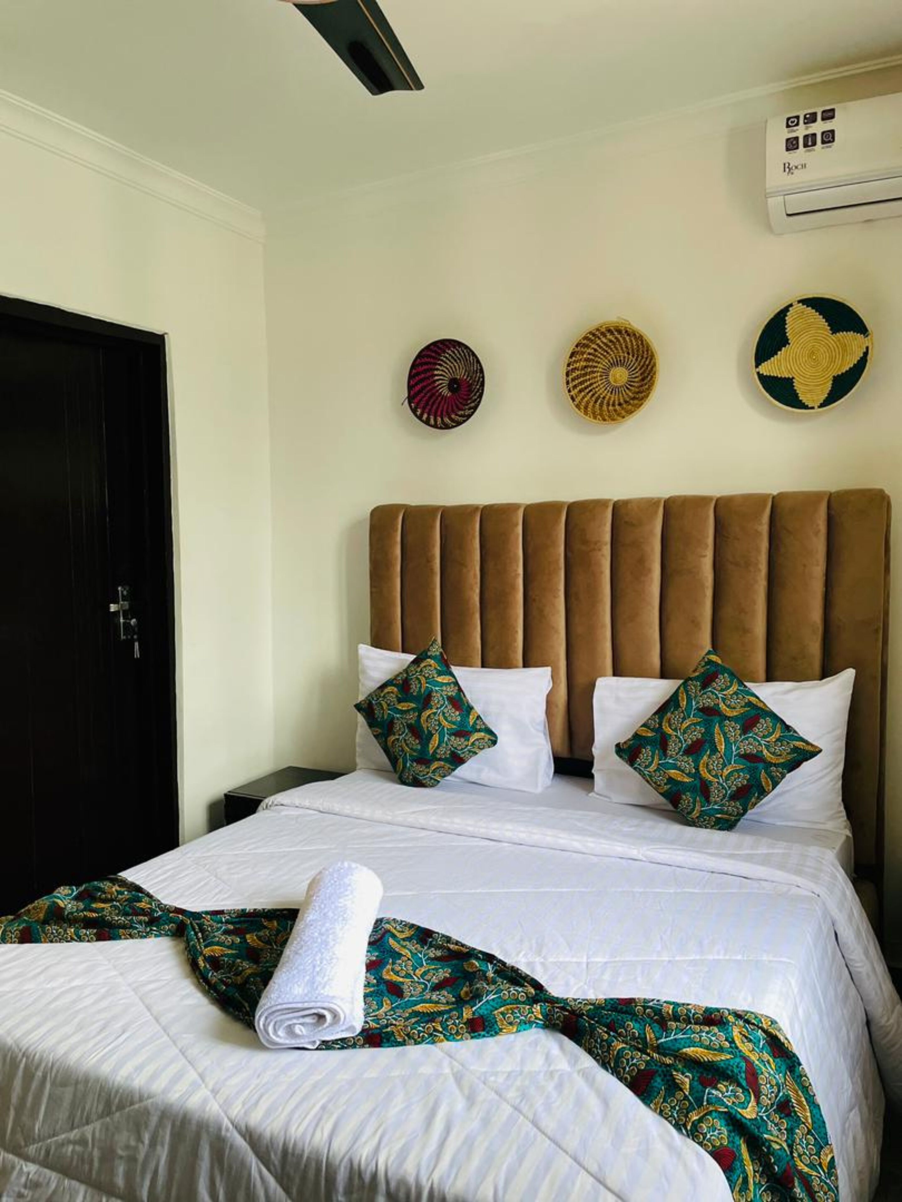 Habitación de hotel con cabecera tapizada en marrón, ropa de cama blanca y almohadas decorativas.