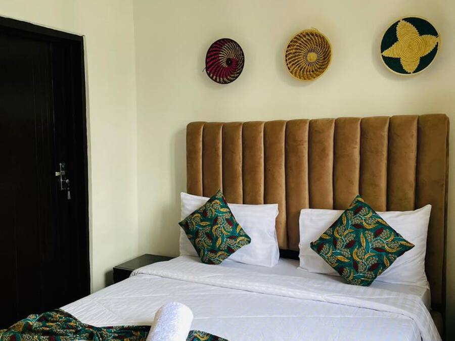 Habitación de hotel con cabecera tapizada en marrón, ropa de cama blanca y almohadas decorativas.