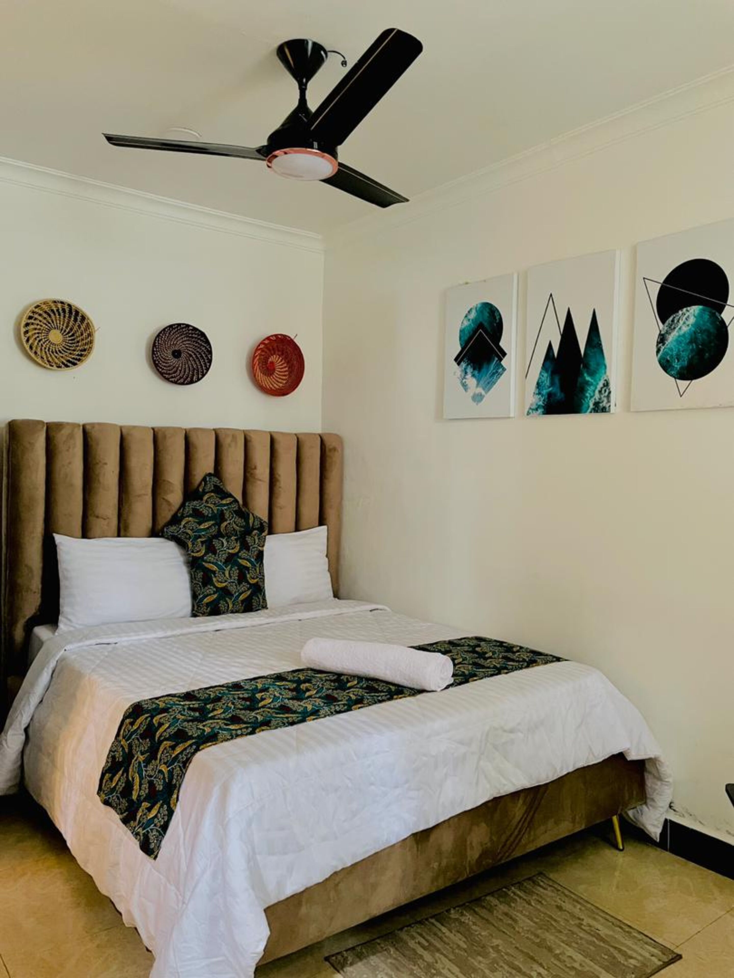 A bedroom with a large bed, a ceiling fan, and three wall art pieces.