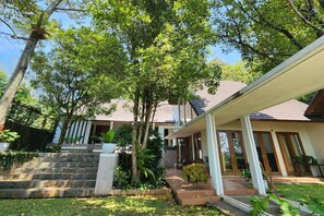 A residential property with a stone staircase leading to a wooden deck, surrounded by lush greenery and a house with a tiled roof. - Villa Rancakendal (Bandung)