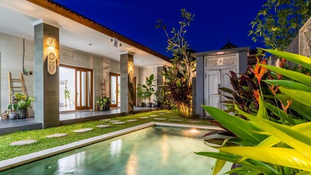 Un área de piscina con una piscina cristalina, rodeada de césped cuidado y plantas en macetas.
