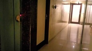 A long, narrow hallway with a door on the left and a door at the end. The floor is tiled, and the walls are plain. - Hotel Shyam Palace (New Delhi)