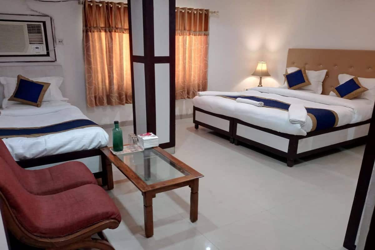 A hotel room with two beds, a glass-top table, a red chair, and a lamp.