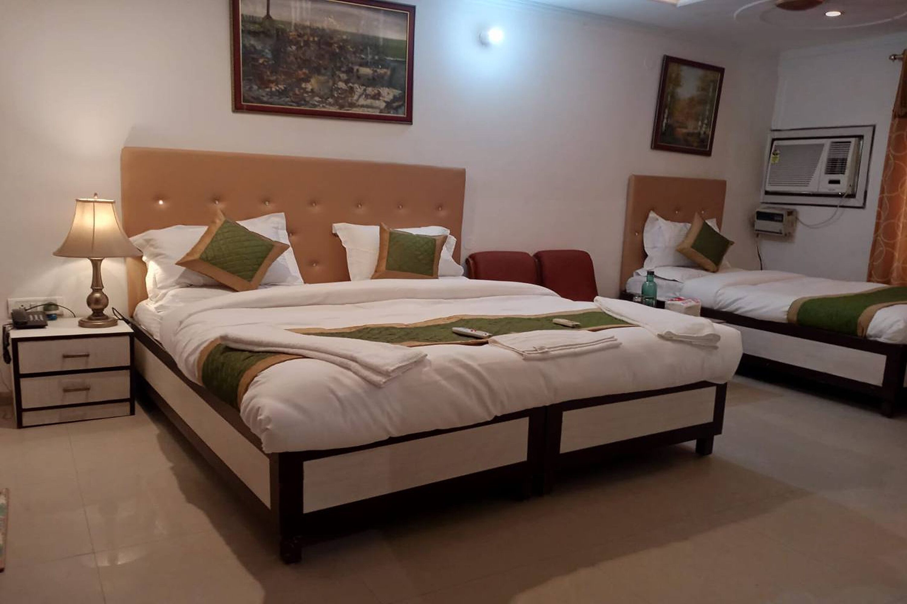 A hotel room with a large bed, a bedside table with a lamp, and a small table with a bottle and glasses.
