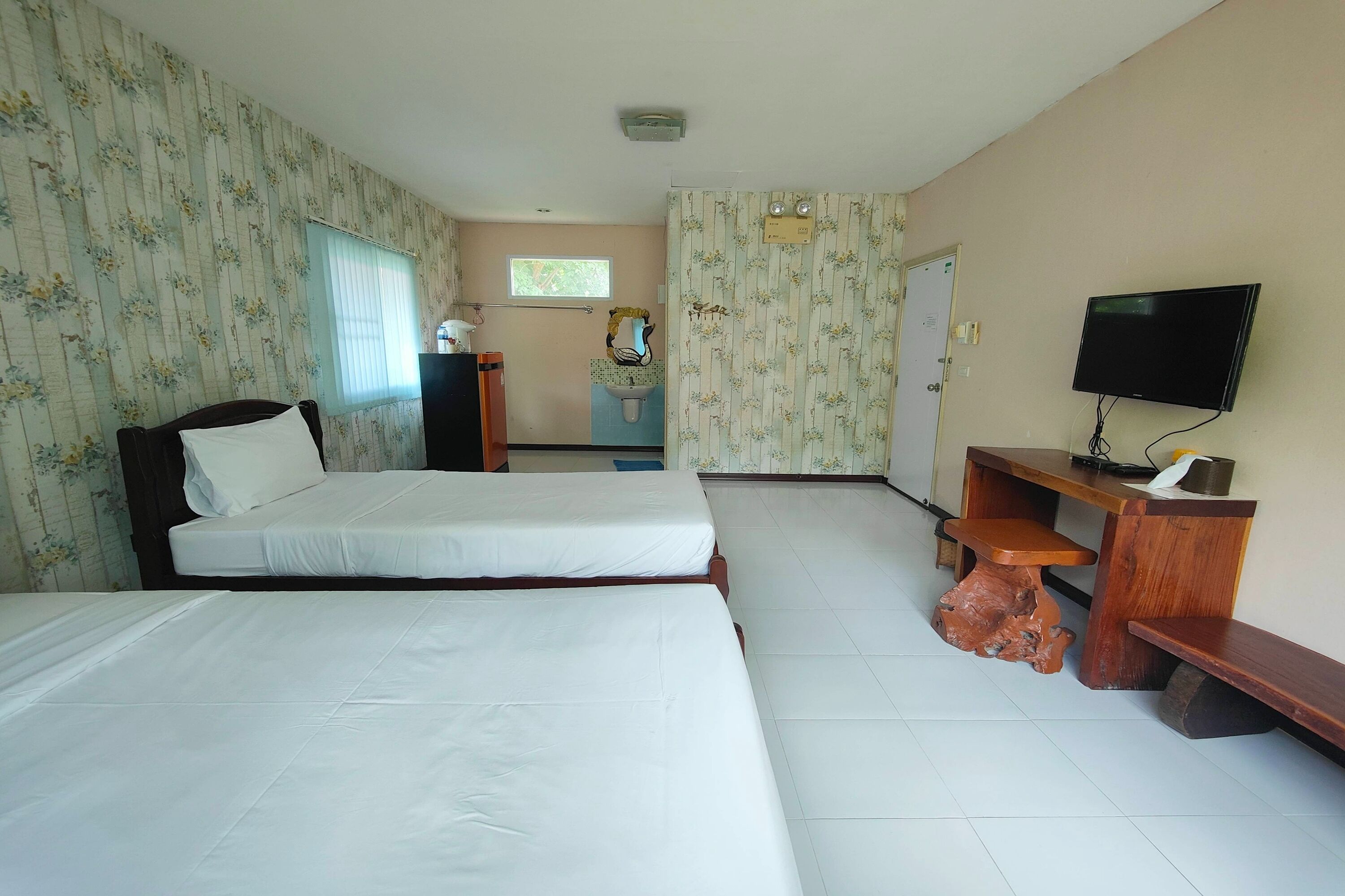 Une chambre d’hôtel avec deux lits, un bureau en bois, une télévision et une salle de bain visible à travers une porte.