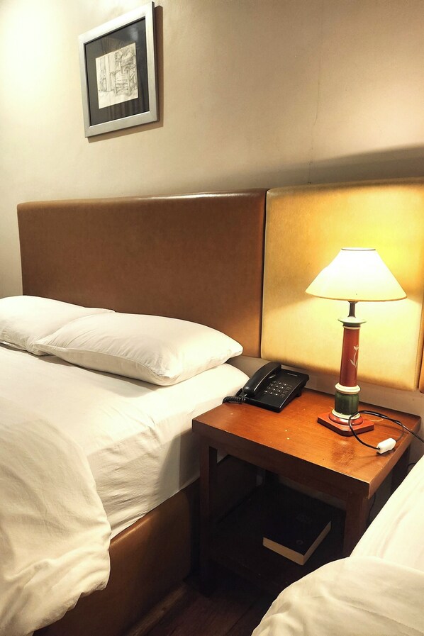 Habitación de hotel con cama, lámpara de noche, teléfono y un cuadro en la pared.
