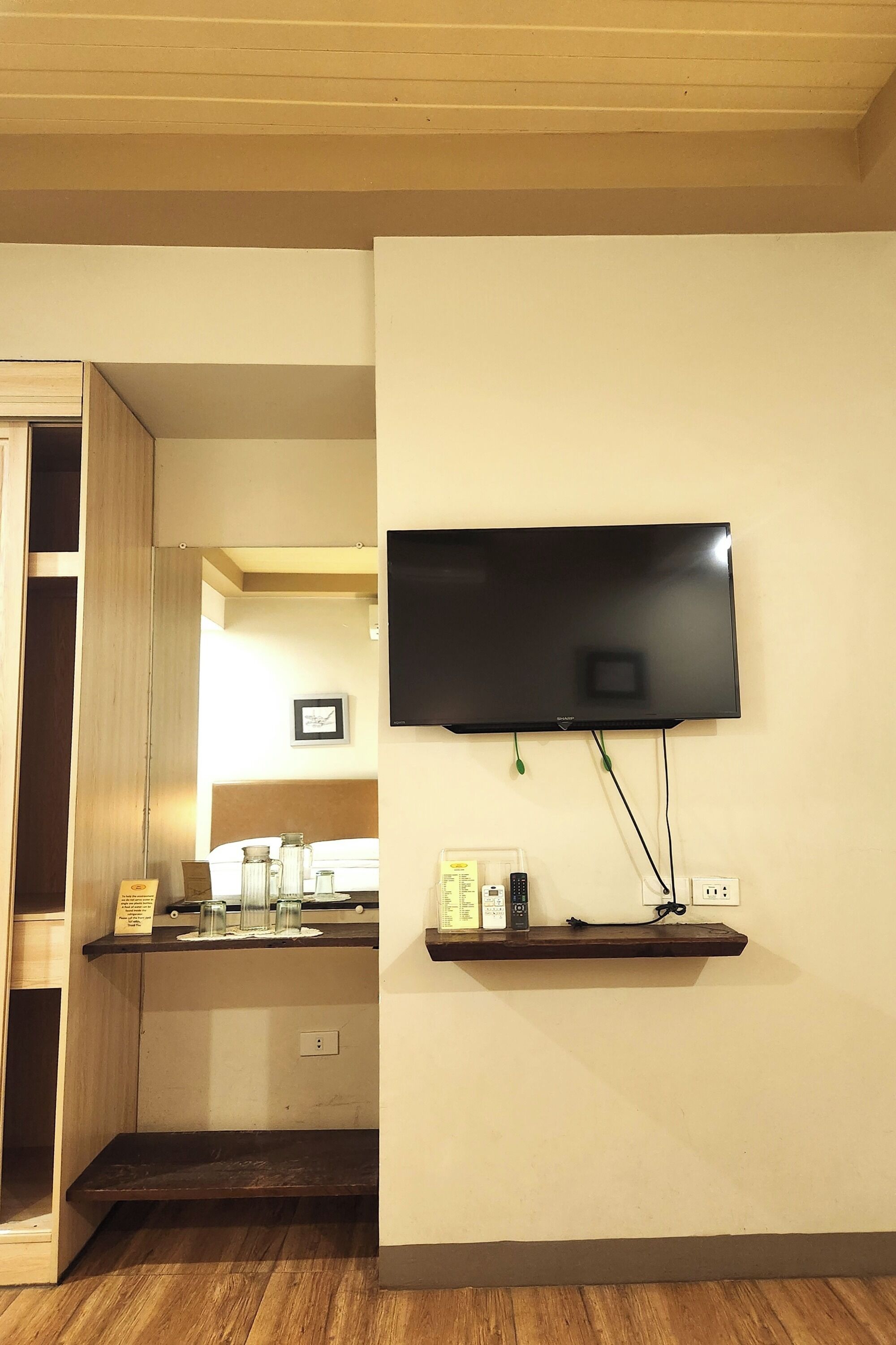A room with a mounted TV on the wall, a wooden shelf with various items, and a wooden floor.