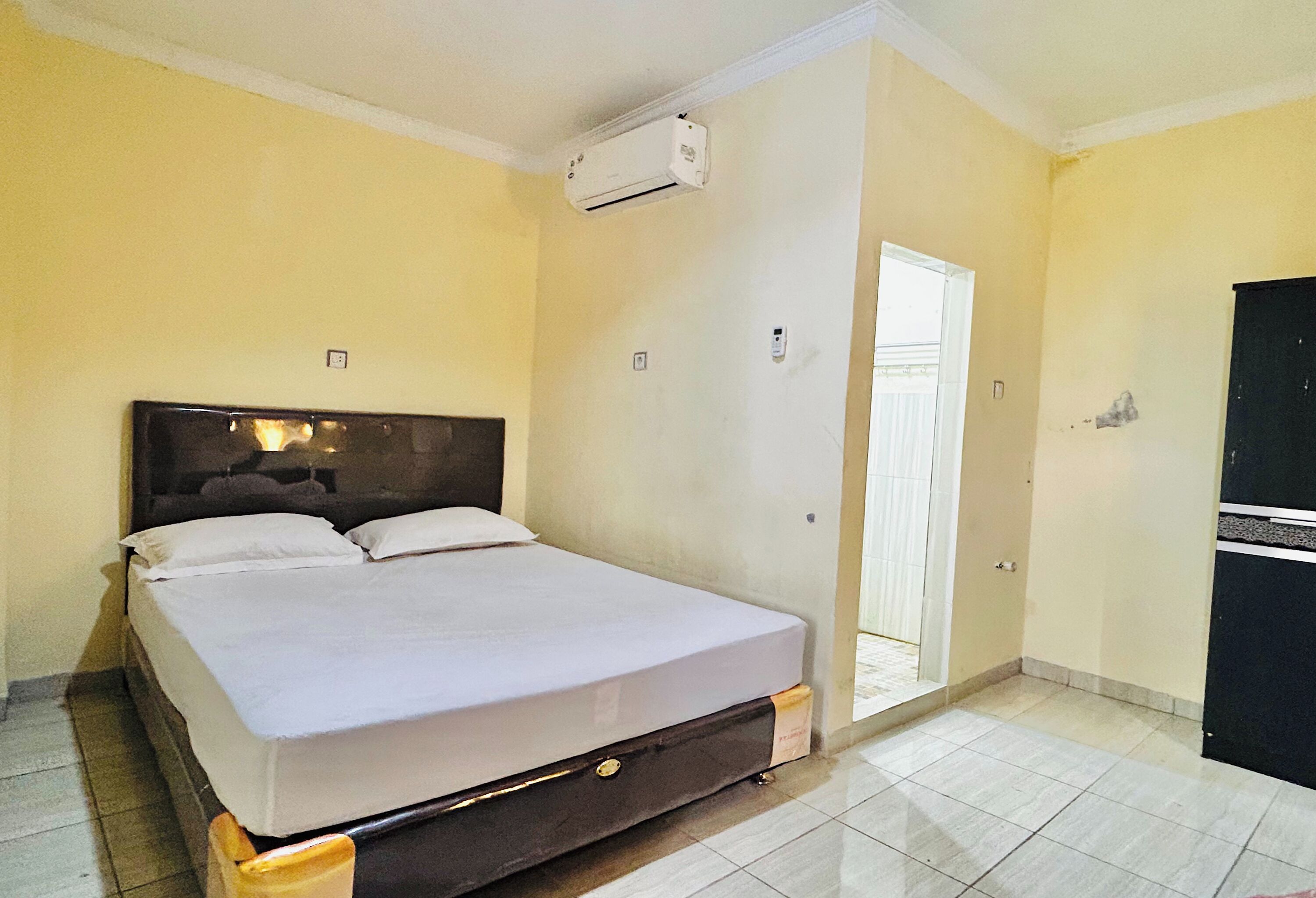 A room with a bed, an air conditioning unit, a door, and a black cabinet.