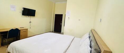 A hotel room with a bed, a desk, a chair, a television, and an air conditioning unit.