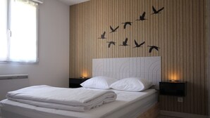 A neatly made bed with white linens, a headboard with a bird silhouette design, and two bedside lamps.