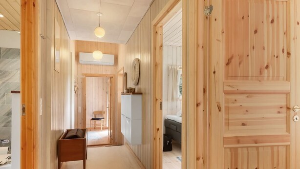 Un pasillo con paredes y puertas de madera, una lámpara en el techo, un escritorio pequeño y una silla.