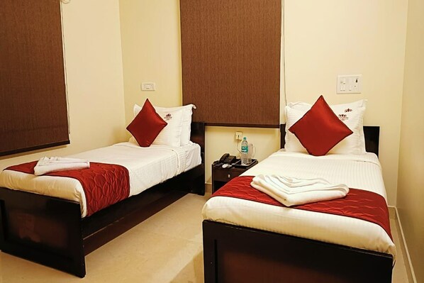 Two single beds with red pillows, a nightstand with a phone and water bottle, and a wall socket.