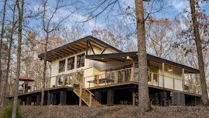 Eine moderne, zweigeschossige Holzhütte mit einer Holzterrasse, großen Fenstern und einer Treppe, die zum Obergeschoss führt.