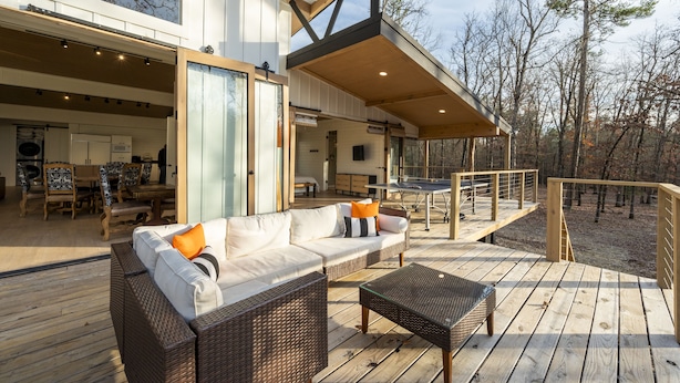 Ein moderner Außenbereich mit Holzterrasse, Korbmöbeln und einer Glastür zu einem Innenraum.
