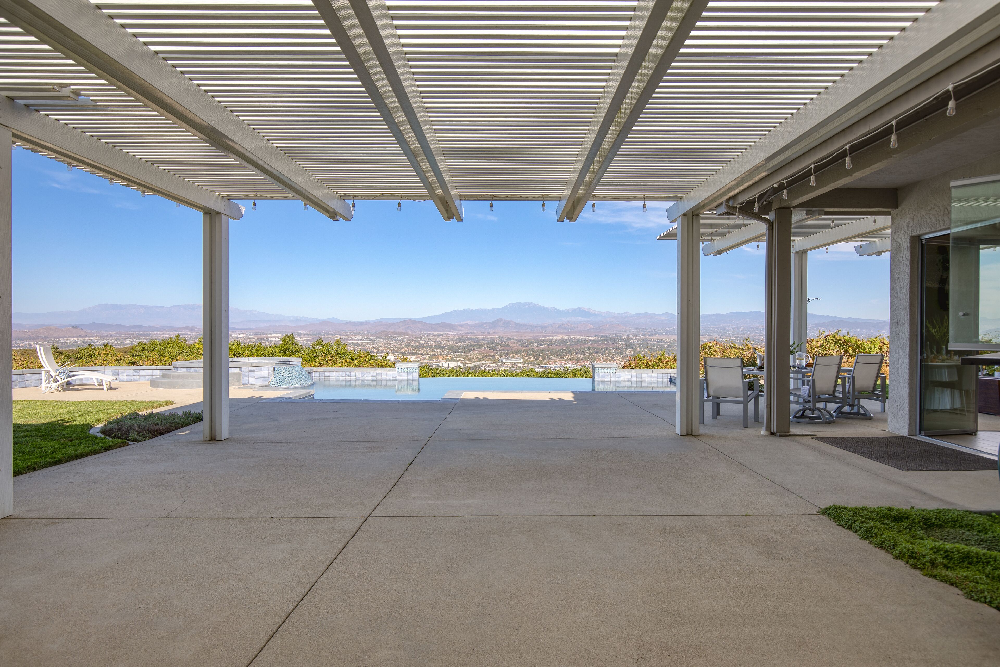 A covered outdoor area with a pool, seating, and a view of mountains.