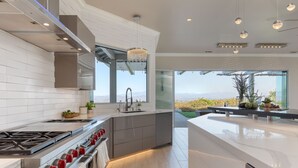 Eine moderne Küche mit einer großen Kochinsel, Edelstahlgeräten und Blick ins Freie.