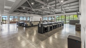 A spacious indoor area with high ceilings, large windows, and a central seating area with sofas and tables.