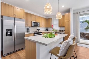 A modern kitchen with stainless steel appliances, wooden cabinets, a central island, and pendant lighting.