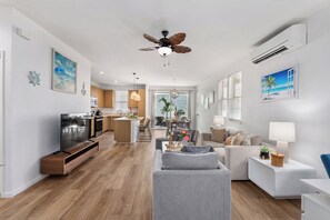 A modern living room with a grey sofa, a TV, and a ceiling fan.