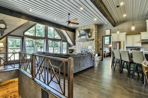 A spacious kitchen with a stone fireplace, wooden ceiling beams, and large windows.