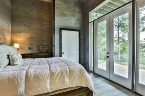 A bedroom with a bed, a nightstand, a lamp, a door, and a view through large glass doors.