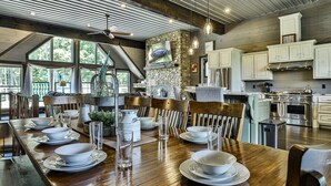 A dining area with a wooden table set for four, a stone fireplace, and modern kitchen cabinets. - Live Love Lake | Blue Ridge, GA (Blue Ridge)
