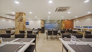 A hotel dining area with marble pillars, tables with black chairs, and a tiled floor. - IRIS HOTEL TIRUPATI (Tirupati)