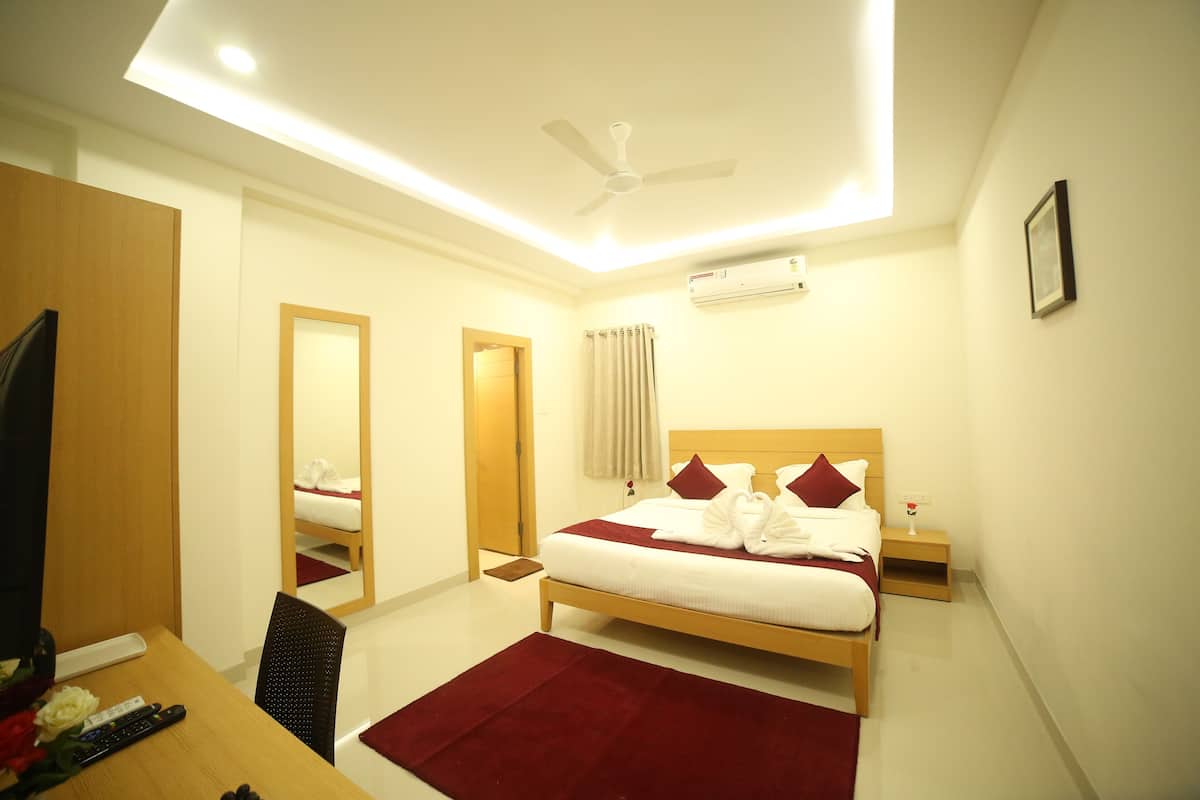 A hotel room with a bed, a desk with a chair, a television, a ceiling fan, and an air conditioning unit.