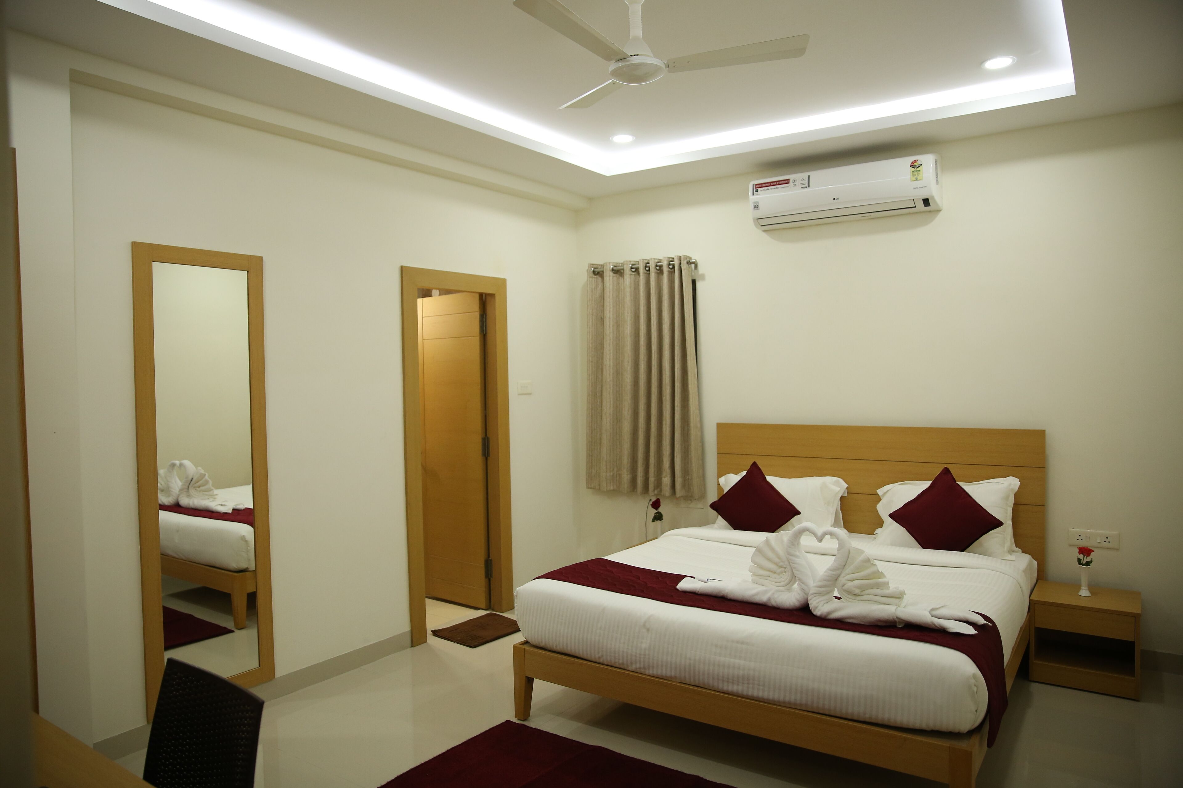 A neatly arranged hotel room with a bed, a bedside table, a mirror, and a ceiling fan.