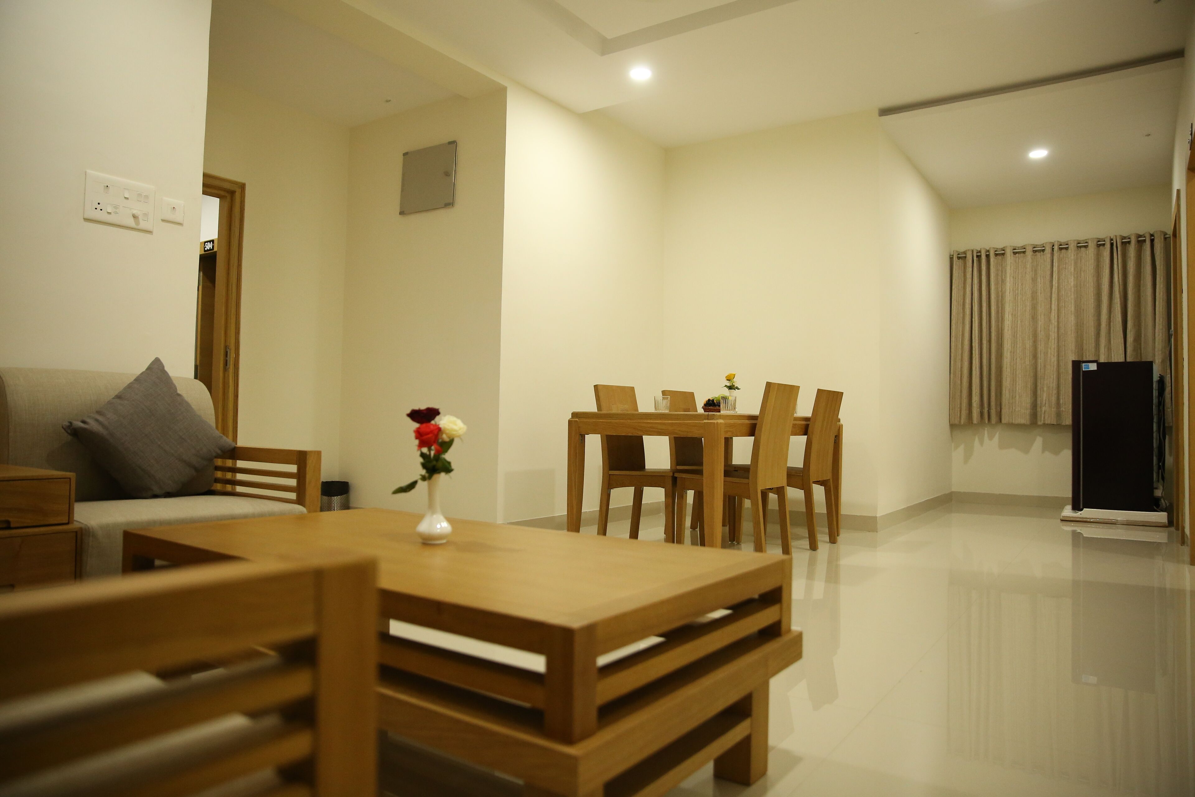 A modern living room with a wooden dining table, chairs, a sofa, and a small decorative vase.