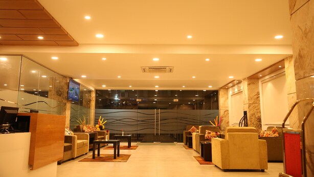 A modern lobby with a reception desk, seating area, and a large glass wall with a cityscape view. - IRIS HOTEL TIRUPATI (Tirupati)