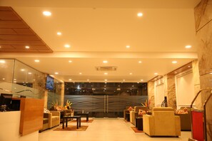 A modern lobby with a reception desk, seating area, and a large glass wall with a cityscape view. - IRIS HOTEL TIRUPATI (Tirupati)