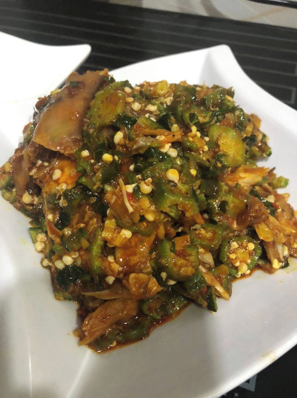A white plate with a dish containing vegetables and meat, garnished with sesame seeds.