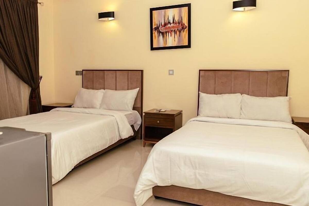 Een hotelkamer met twee bedden, een klein nachtkastje, een kunstwerk aan de muur en een gordijn aan de linkerkant.