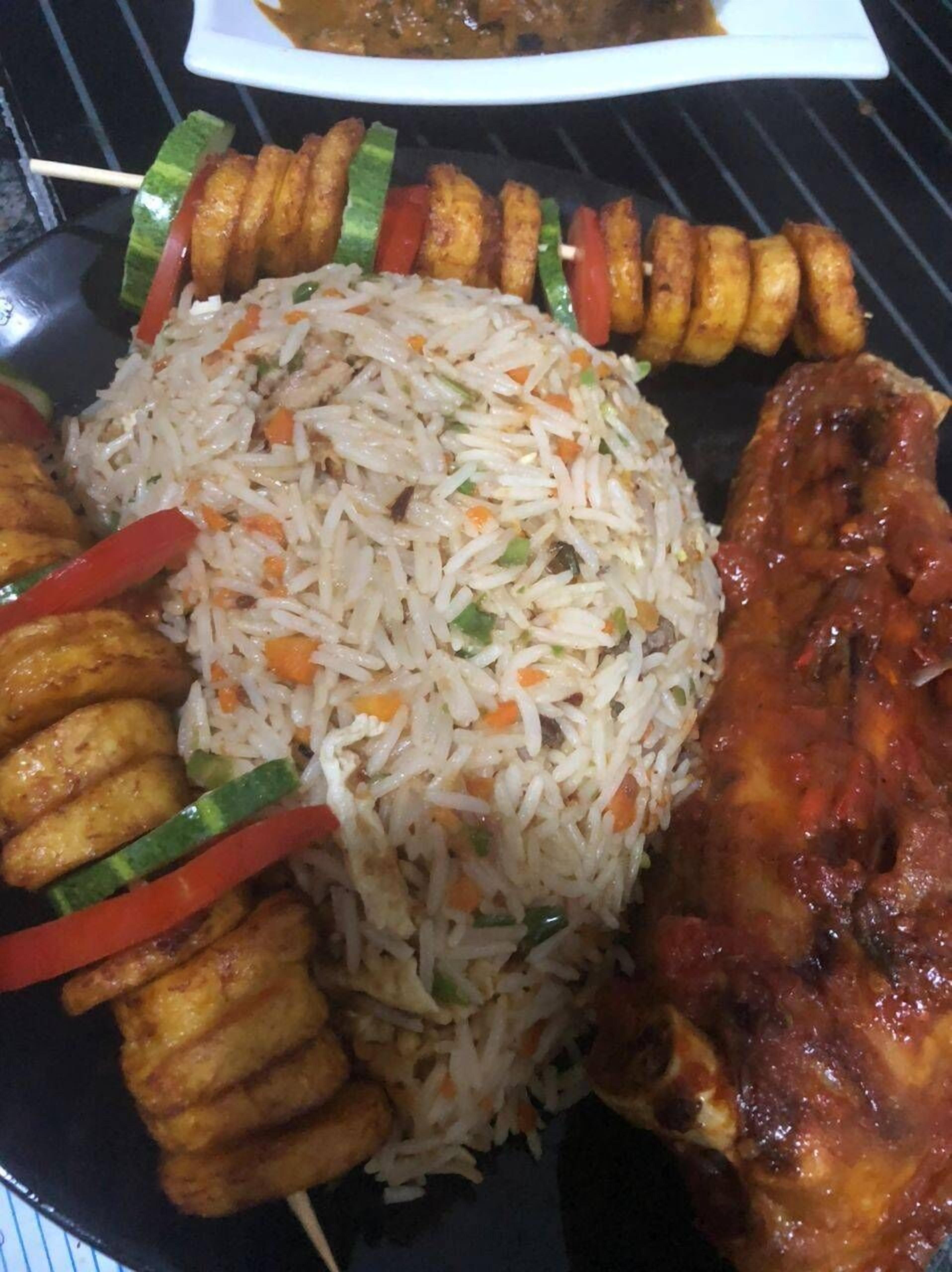 A plate of fried rice with vegetables, skewered meat, and fried plantains.