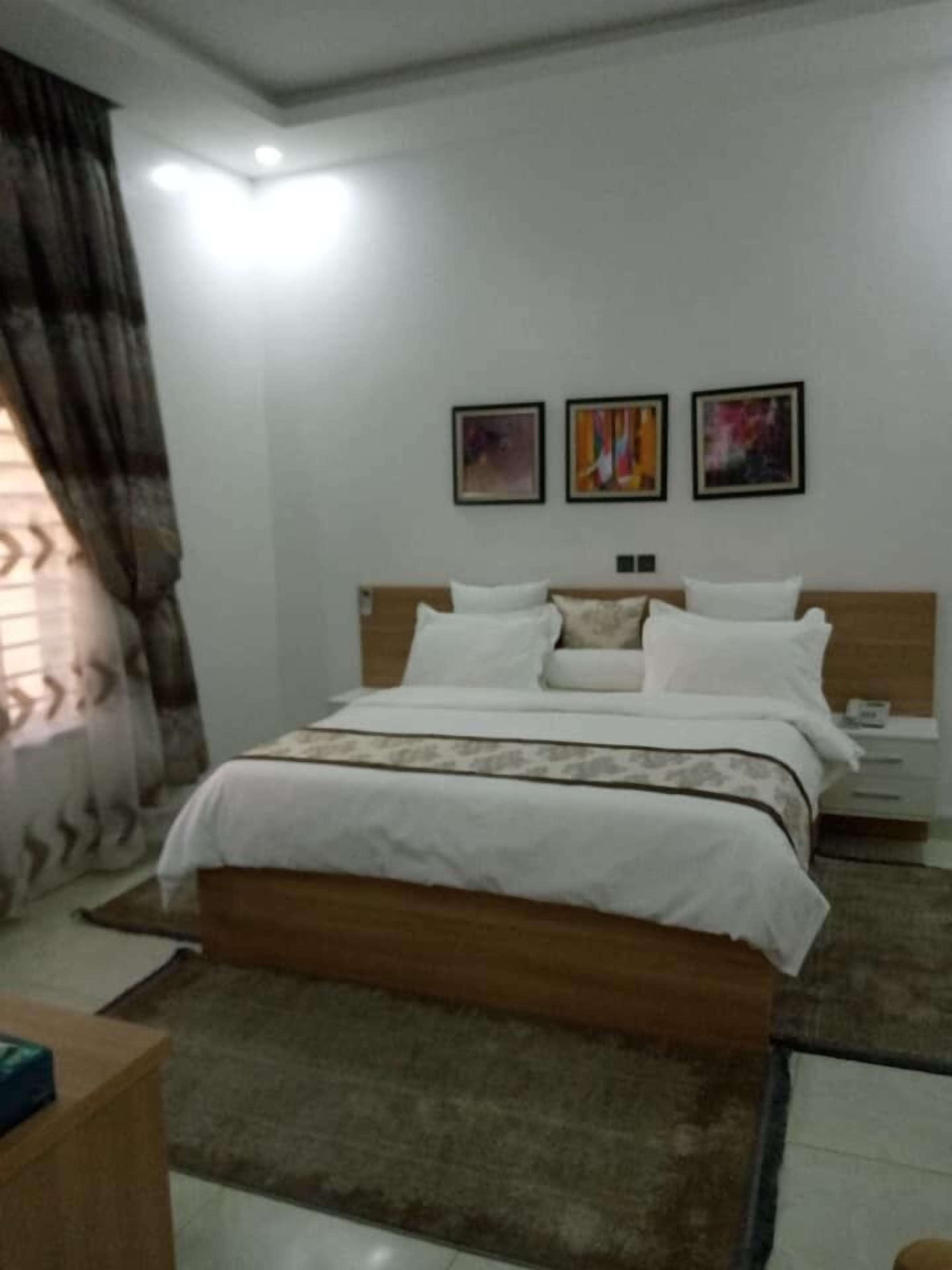 A bedroom with a bed, a nightstand, and a window with curtains. There are three framed pictures on the wall.