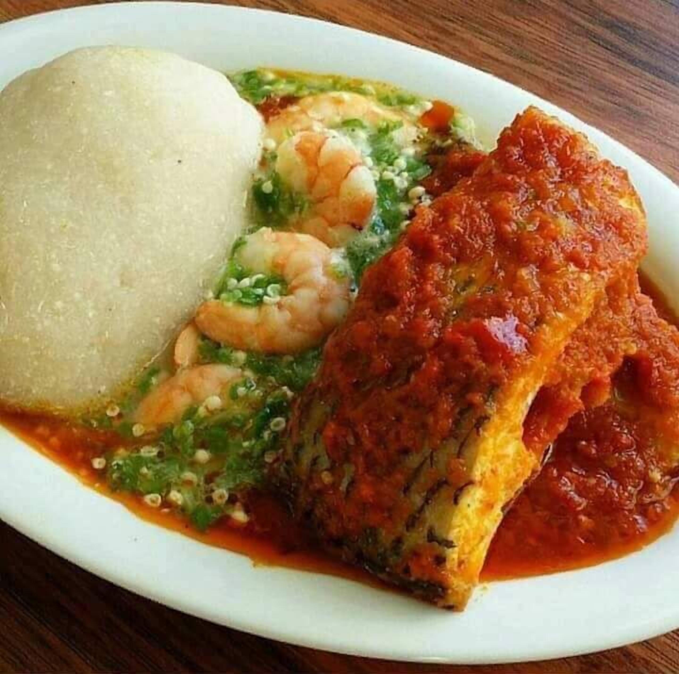 A plate with a fish, shrimp, and a white food item, possibly fufu, served with a tomato-based sauce.