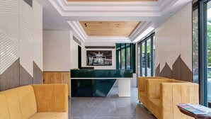 A reception area with a modern design, featuring a reception desk, two yellow sofas, and a large window providing a view of the outdoors. - Baga Bliss by Celestiial Hospitality (Calangute)