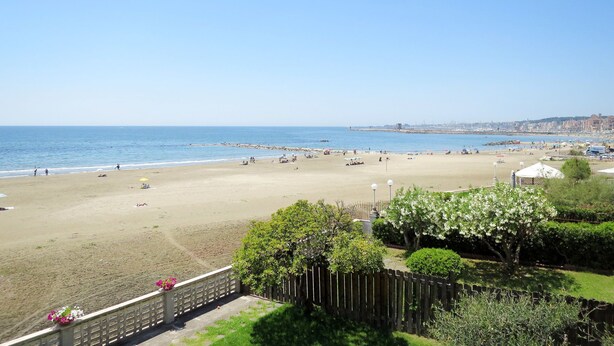 A beach with a wooden fence, a clear sky, and a distant cityscape. - Vacation home Randi by Interhome (Anzio)