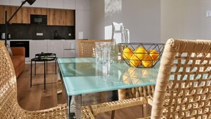 Una cocina moderna con armarios blancos, encimera negra y mesa de vidrio con sillas de mimbre.