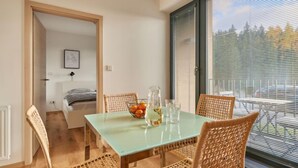 Un comedor con una mesa de vidrio, sillas de mimbre, un frutero y vistas amplias a través de grandes ventanales.