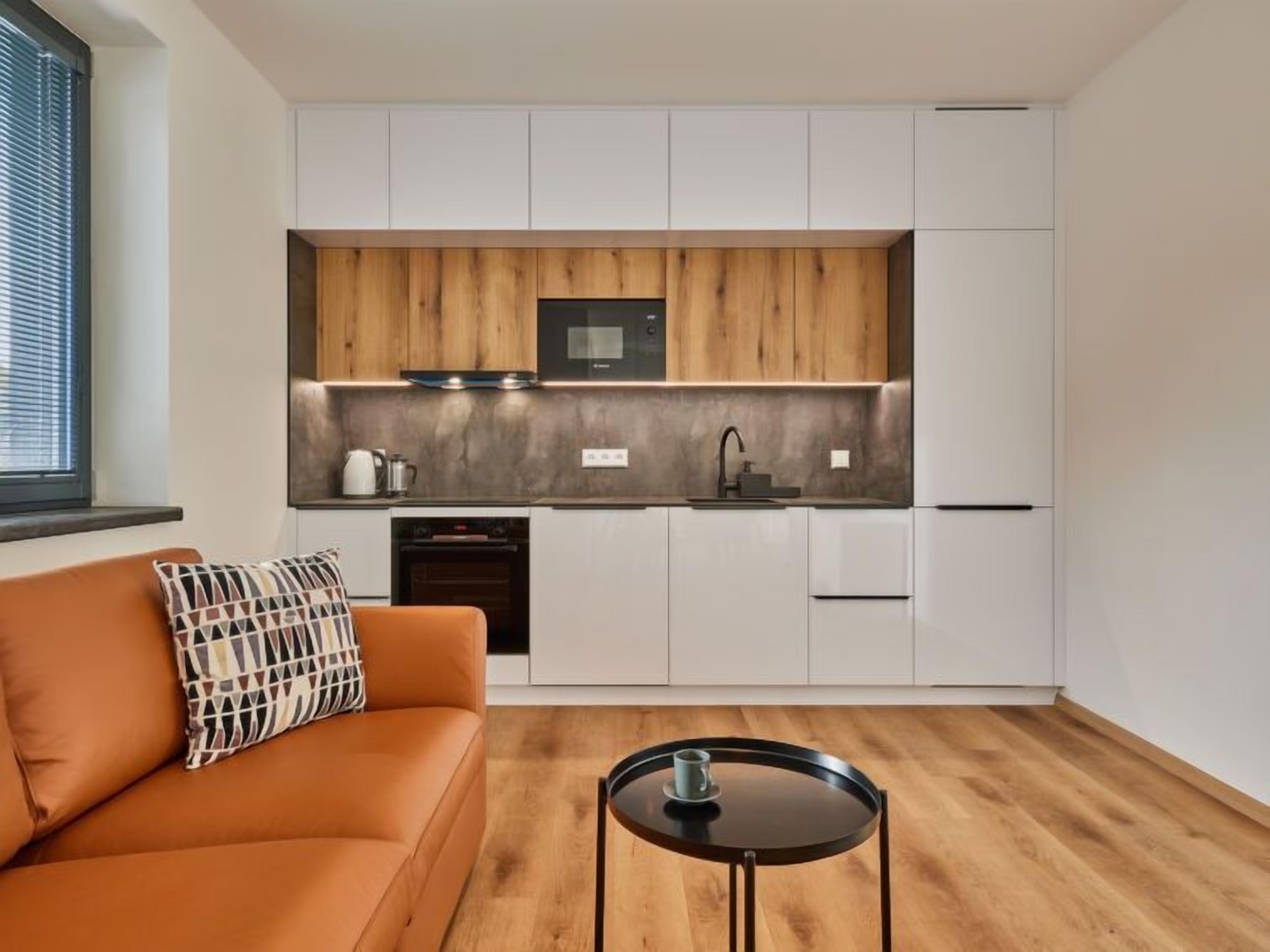 A compact kitchen with white cabinets, a wooden accent wall, a built-in oven, and a black microwave.