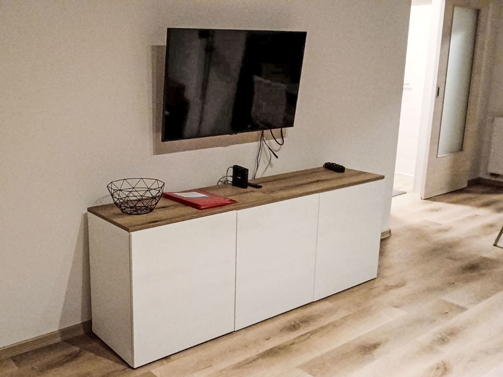 En moderne stue med et fladskærms-tv på væggen, et træsofabord og et hvidt skab.