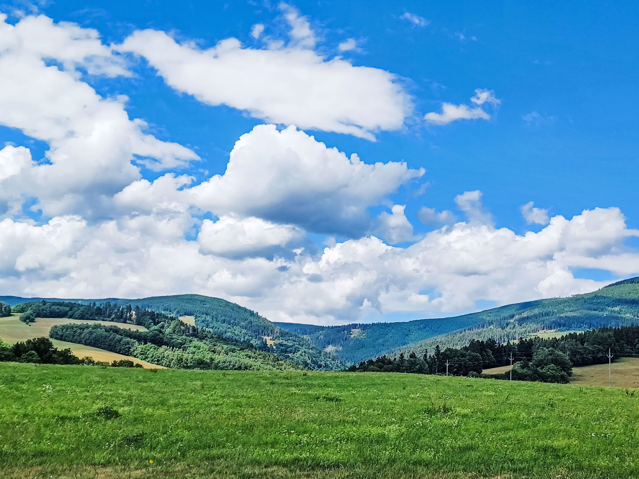 A panoramic view of a green valley with rolling hills and a clear blue sky with clouds.